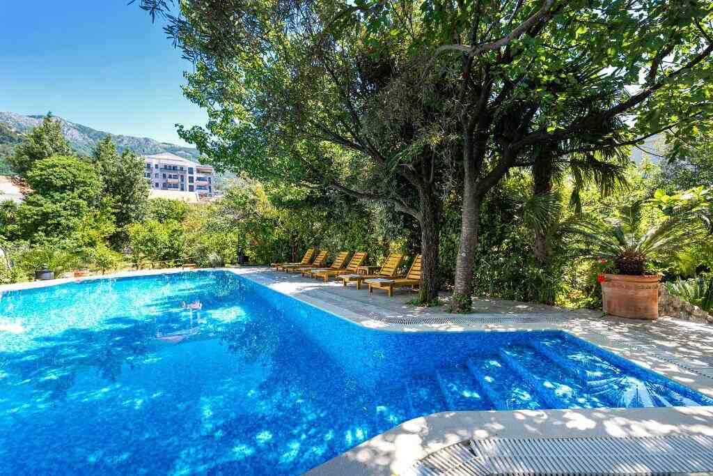 Pool terrace with sun loungers under trees at Hotel Dubrava